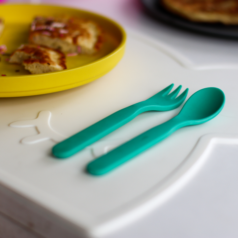 Free from melamine, and biodegradable and compostable, our plant-based spoon and fork cutlery set makes mealtimes (and sneaky snacks) way more fun! Green cutlery set displayed on toddler table next to yellow plate of food.