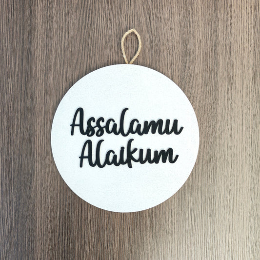 Round white sign with 'Assalamu Alaikum' text on a wooden background