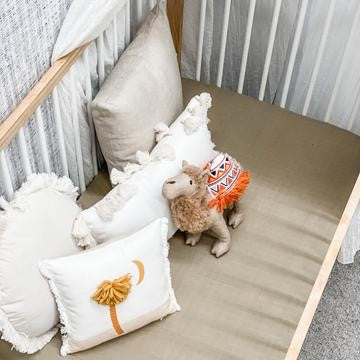 100% Organic Cotton Muslin Baby Bedding Set in Sand Dune color - Soft, Breathable, and Lightweight. Perfect for cribs and bassinets. Coordinates beautifully in nurseries. Suitable from newborn to toddler stage. Sheets displayed on a cot in a staged nursery close-up.