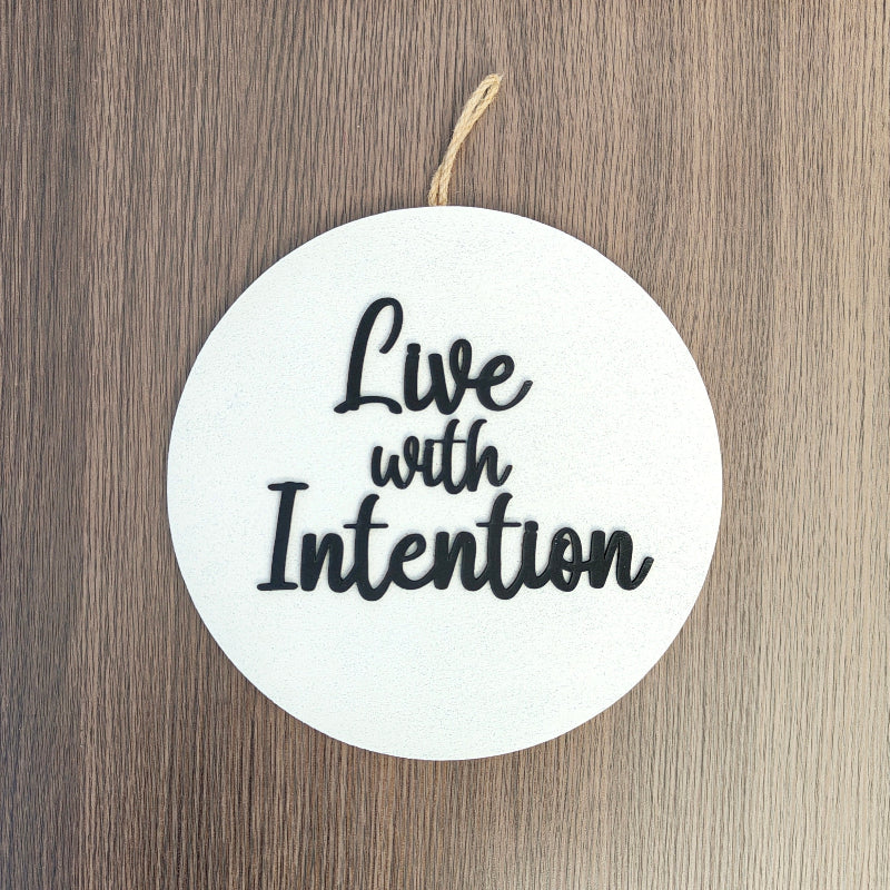 Round white sign with 'Live with Intention' text on a wooden surface