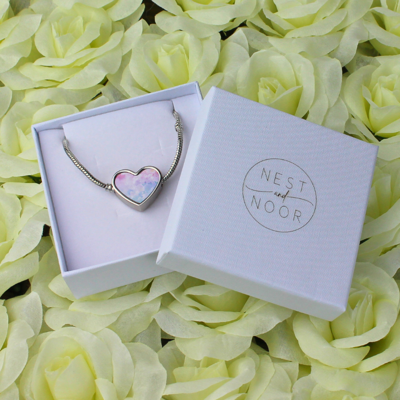 Heart-shaped charm with pink and blue pastel print and silver bracelet in a white gift box.