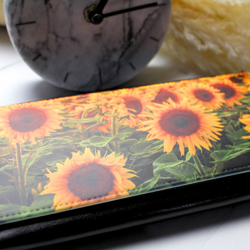 Vegan leather purse with sunflowers in a field print on marble clock and feather plant background