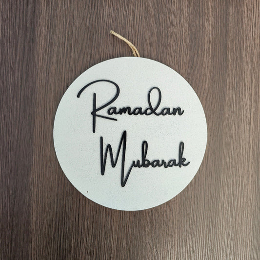 Round white sign with 'Ramadan Mubarak' text on a wooden surface