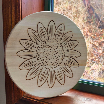 Round wooden board with engraved sunflower design.