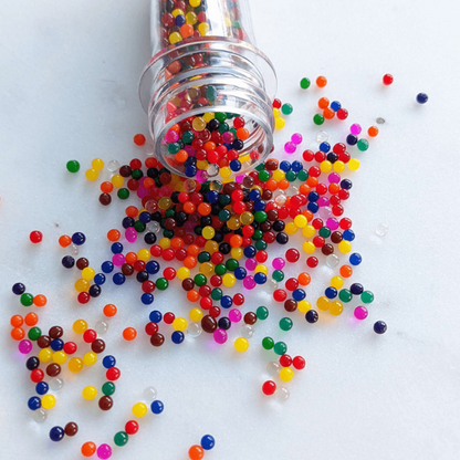 Discover our vibrant rainbow water beads! These reusable and certified water beads provide hours of sensory play. Non-toxic, biodegradable, and safe for kids above 5. Dehydrated beads spilling out of container onto white surface.
