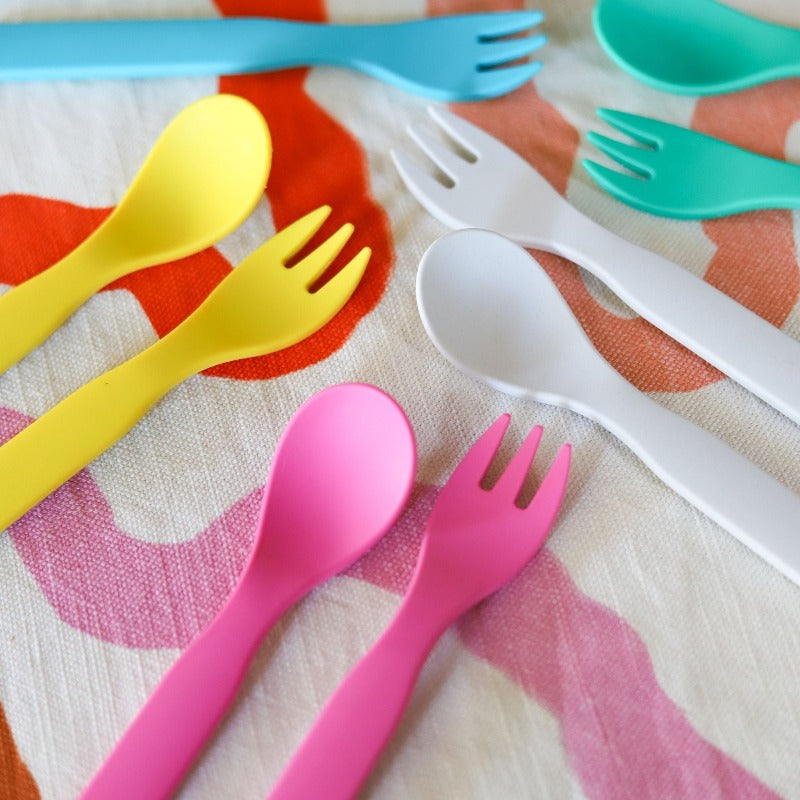 Free from melamine, and biodegradable and compostable, our plant-based spoon and fork cutlery set makes mealtimes (and sneaky snacks) way more fun! 5 colours of cutlery sets displayed on a tea towel.