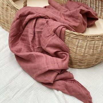 Experience pure comfort with 100% Organic Cotton Lightweight Muslin Baby Swaddle Wraps. Discover stunning colours & large size for versatile use. Red swaddle draped over wicker bassinet.