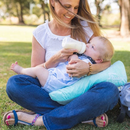 Feeding Friend Nursing Pillow - The Perfect Gift for Hassle-Free Baby Feeding. Woman bottle feeding baby in the park.
