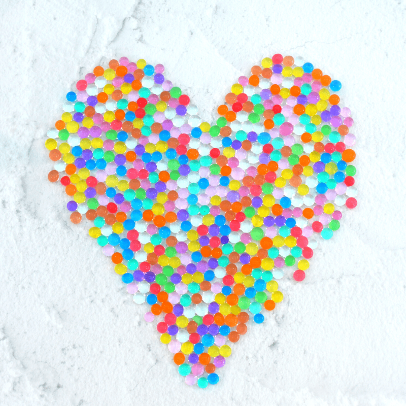 Discover our vibrant rainbow water beads! These reusable and certified water beads provide hours of sensory play. Non-toxic, biodegradable, and safe for kids above 5. Hydrated water beads displayed in a heart shape.